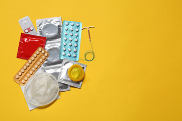 Contraceptive pills, condoms and intrauterine device on yellow background, flat lay with space for text. Different birth control methods