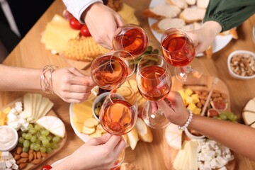 People clinking glasses with rose wine above wooden table, closeup