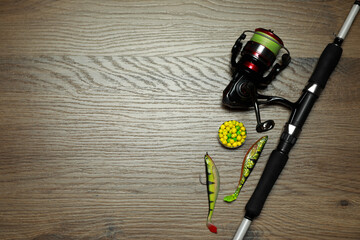 Fishing rod with spinning reel and baits on wooden background, flat lay. Space for text