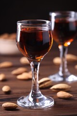 Liqueur glass with tasty amaretto and almonds on wooden table, closeup