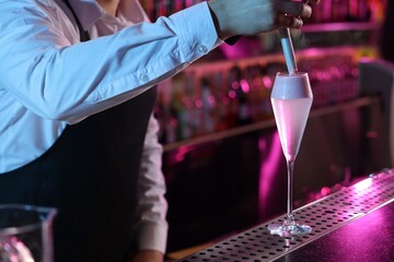 Bartender adding foam onto alcoholic cocktail at counter in bar, closeup