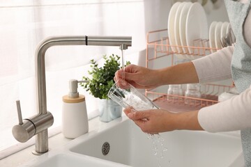 Woman washing glass at sink in kitchen, closeup - obrazy, fototapety, plakaty