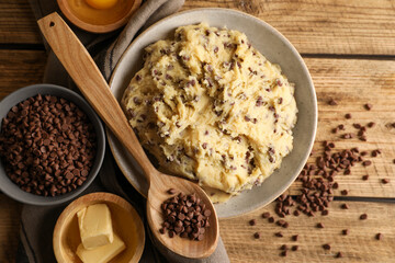 Chocolate chip cookie dough in bowl and ingredients on wooden table, flat lay