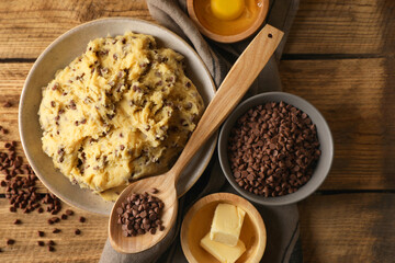 Chocolate chip cookie dough in bowl and ingredients on wooden table, flat lay