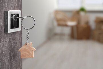 Mortgage and real estate. Open door with key and house shaped keychain against blurred background,...