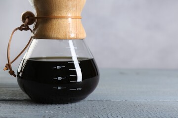 Glass chemex coffeemaker with tasty drip coffee on grey wooden table, closeup. Space for text