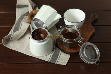 Moka pot, cup, ground coffee and kitchen towel on wooden table