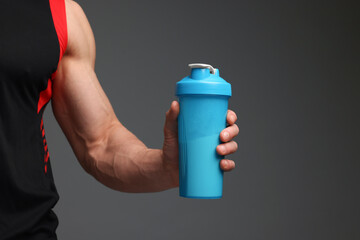 Young man with muscular body holding shaker of protein on grey background, closeup. Space for text