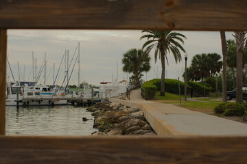 View south out wood pavilion at Demens Landing Park. Through wood rectangles out to marina with...