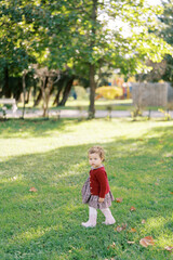 Little girl walks on the green grass in the garden with her head turned to the side