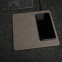 Charging the smartphone with leather wireless charger on desk. Gray color leather charger pads....