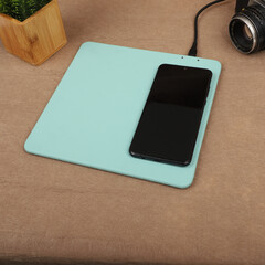 Charging the smartphone with leather wireless charger on desk. Teal leather charger pads. Wireless...