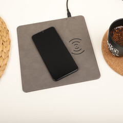 Charging the smartphone with leather wireless charger on desk. Gray color leather charger pads....