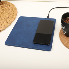 Charging the smartphone with leather wireless charger on desk. Blue color leather charger pads....