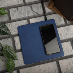 Charging the smartphone with leather wireless charger on desk. Blue color leather charger pads....