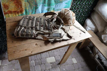 A military helmet of a Ukrainian soldier with a heavy bulletproof vest on wooden table in checkpoint dugout interior