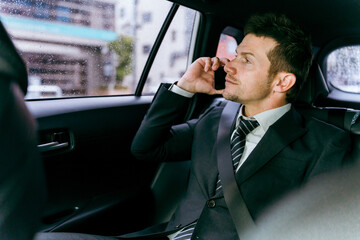 タクシーに乗りながら電話する欧米人ビジネスマン
