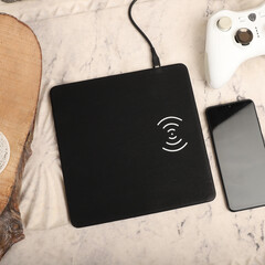 Charging the smartphone with leather wireless charger on desk. Black color leather charger pads. Wireless mousepad, Charger pad. Closeup, top view, no people. Concept shoot. Gamepad controller view.