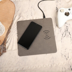 Charging the smartphone with leather wireless charger on desk. Gray color leather charger pads....