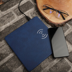 Charging the smartphone with leather wireless charger on desk. Blue color leather charger pads. Wireless mousepad, Charger pad. Closeup, top view, no people. Concept shoot. © ismailbasdas