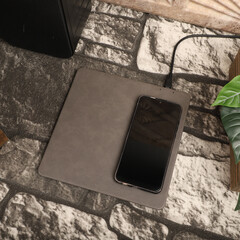 Charging the smartphone with leather wireless charger on desk. Gray color leather charger pads....
