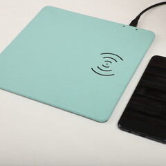 Charging the smartphone with leather wireless charger on desk. Teal leather charger pads. Wireless...