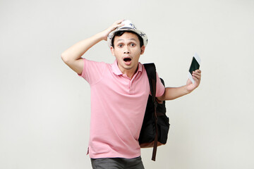 Asian man backpacker holding passport and airline ticket with shocked and surprised expression. digital nomad and travelling concept. on isolated background
