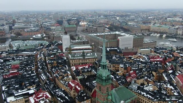 Drone view in Stockholm, Sweden. Flying away from the old city with classic style yellow buildings with snow on their roofs, a church and the royal palace