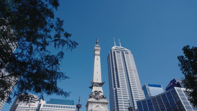 Indianapolis soldiers and sailors memorial in monument circle with modern high rise skyscrapers reveal from behind park tree