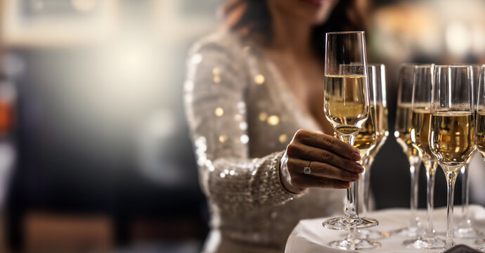 A bartender holds a plate with pink champagne and a woman in a cocktail dress takes one of the glasses at an event, party or wedding