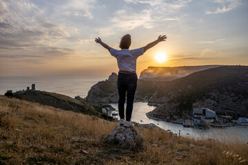 Happy woman on sunset in mountains. Woman standing with her back on the sunset in nature in summer...