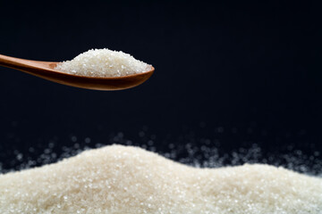 Wooden spoon with sugar crystals on black background