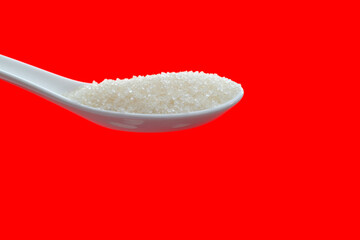 Ceramic spoon with sugar crystals on red background