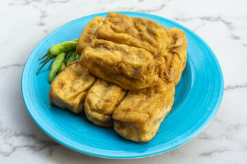 Deep fried tofu on blue plate served with cayenne peppers on marble table. 