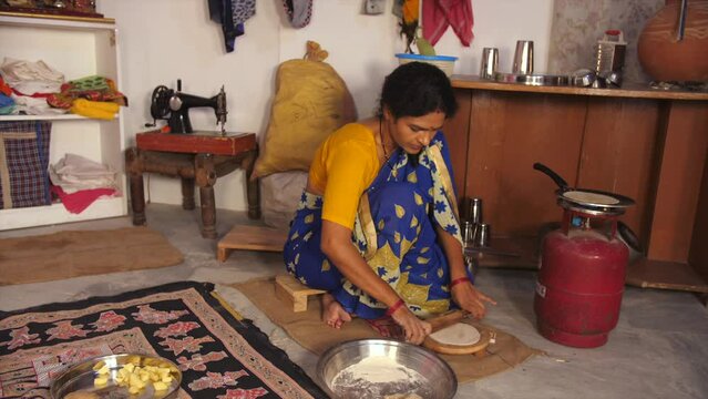 A middle-aged woman is rolling wheat dough with a rolling pin - temporary kitchen  poor family  daily wage help. An Indian housewife is making Rotis / Chapatis for her family members - rural househ...