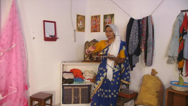 A middle-aged woman is performing Aarti at home - aarti thali  incense stick  morning prayers  religious woman  lord statue  positive aura. An Indian female is doing puja - mini temple at home  mor...