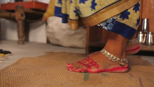 A closeup shot of a woman wiping her bare feet on a rucksack doormat - cleanliness and hygiene  house rules. A rural household in an Indian village - a poor family  a single lady  BPL  wearing paya...