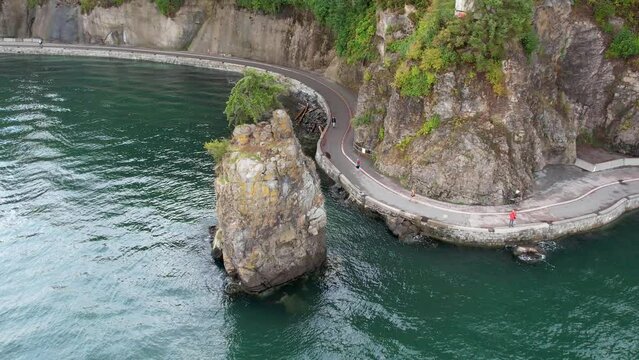 Siwash Rock, Seawall in Stanley Park during Dramatic Sky on West Coast of Pacific Ocean. Downtown Vancouver, BC, Canada. Nature Background. Slow Motion. Aerial video of the shoreline with people.