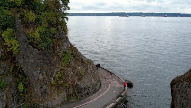 Siwash Rock, Seawall in Stanley Park during Dramatic Sky on West Coast of Pacific Ocean. Downtown Vancouver, BC, Canada. Nature Background. Slow Motion. Aerial video of the shoreline with people.
