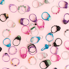 Multicolored handmade rings made of wire and natural stones scattered on a pink background.