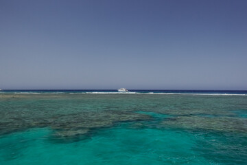 large coral reef with turquoise water and a single boat with blue sky