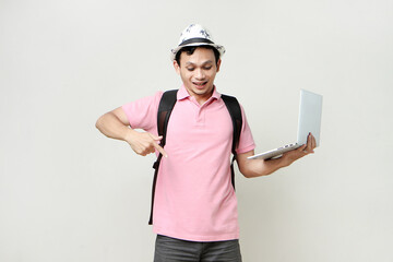 Asian man backpacker holding laptop computer with pointing finger gesture. digital nomad and...
