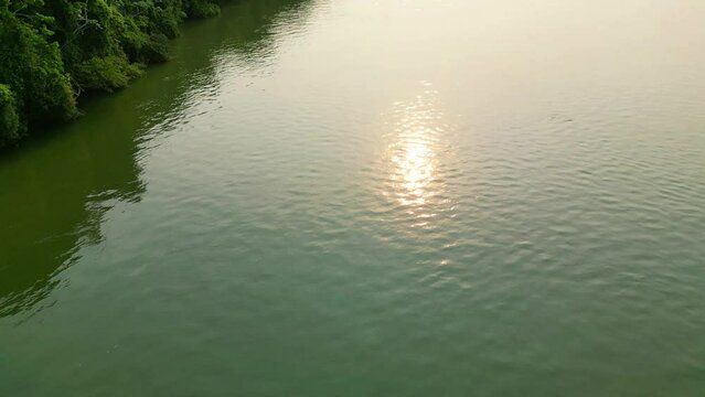 A beautiful view of the sun reflecting on the water next to the green coast