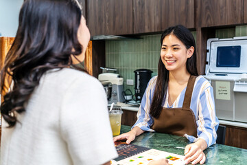 Smiling young asian waitress in a cafe with customer for service, payment or order on counter at...