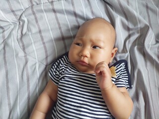 A cute baby with a natural expression wearing a striped shirt, lying on the bed