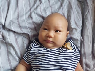 A cute baby with a natural expression wearing a striped shirt, lying on the bed