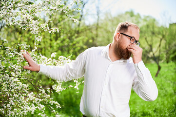 Man allergic suffering from seasonal allergy at spring in blossoming garden at springtime. Bearded...