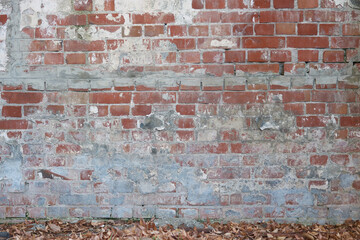 Weathered and worn old brick wall which has been repaired. The are fallen leaves by it.
