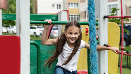 A cute little girl is playing in the children's yard. Healthy summer fun for kids. Child girl...
