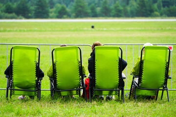 Four green folding chairs with spectators at the edge of a green field waiting for the show to start